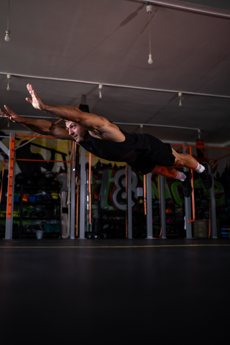 Man performing a Superman-style exercise in a gym, arms and legs extended as he flies parallel to the floor.