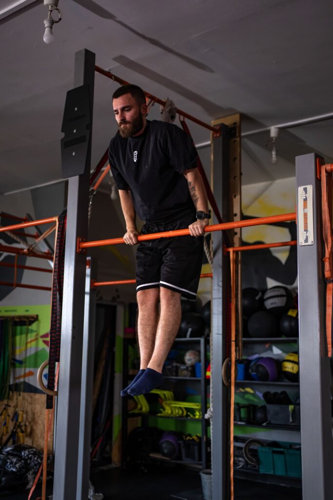 Bearded man in a black shirt and shorts doing a pull-up on an orange gym bar.