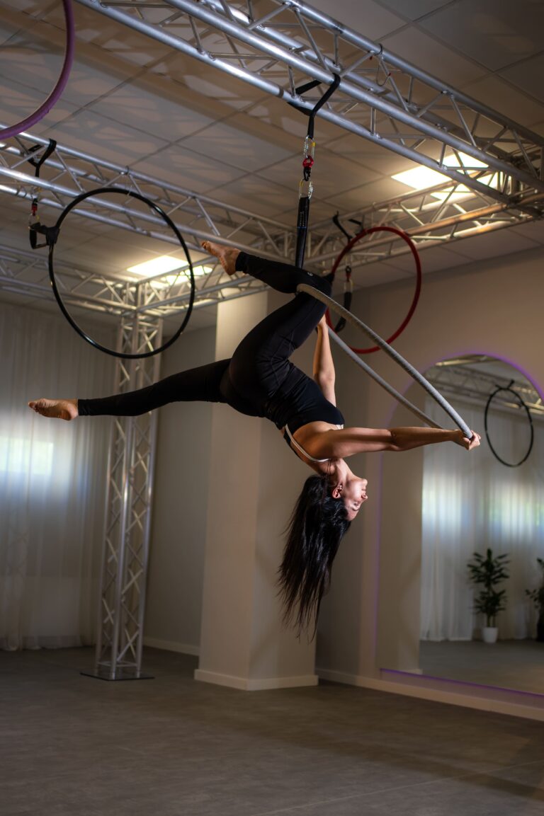 Aerialist hanging upside down from a fabric suspended from metal truss in a studio.